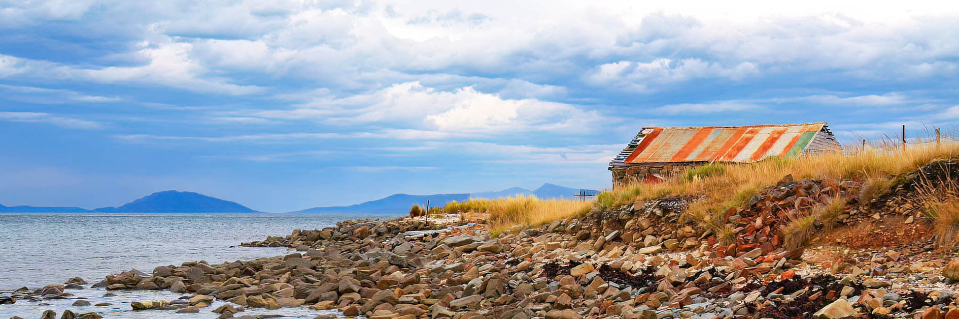 Rustic building on a rocky coastline with a lake and sky in the background