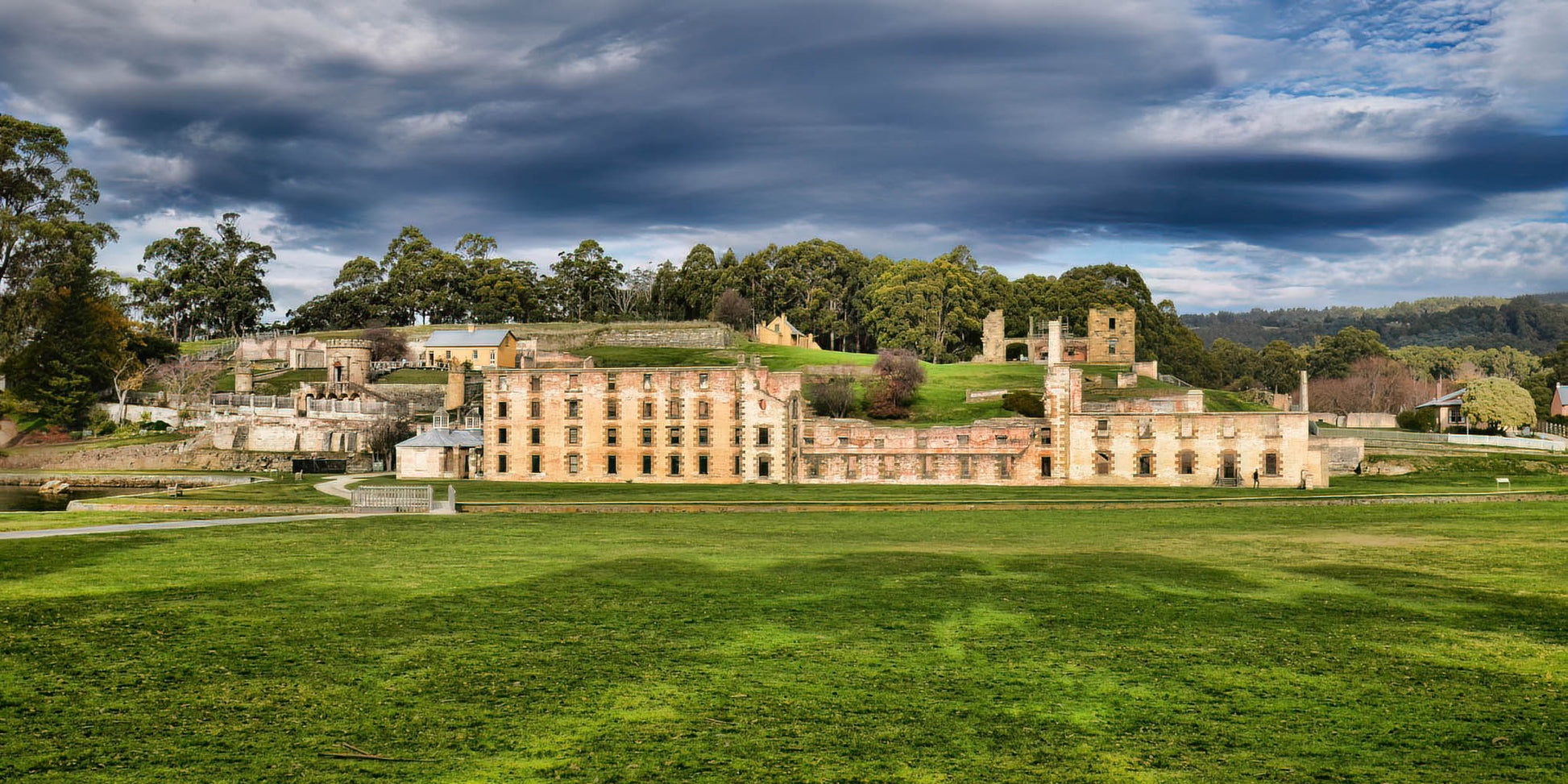 Historic Port Arthur Prison complex with green grass and trees under a cloudy sky