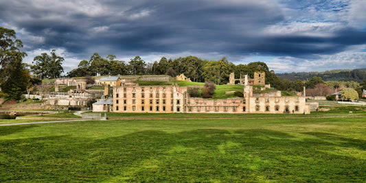 Historic Port Arthur Prison complex with green grass and trees under a cloudy sky