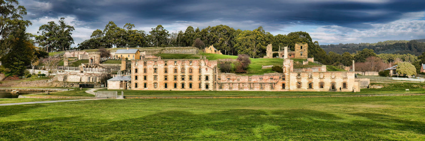 Panoramic view of a historic building at Port Arthur with green grass and trees in the foreground
