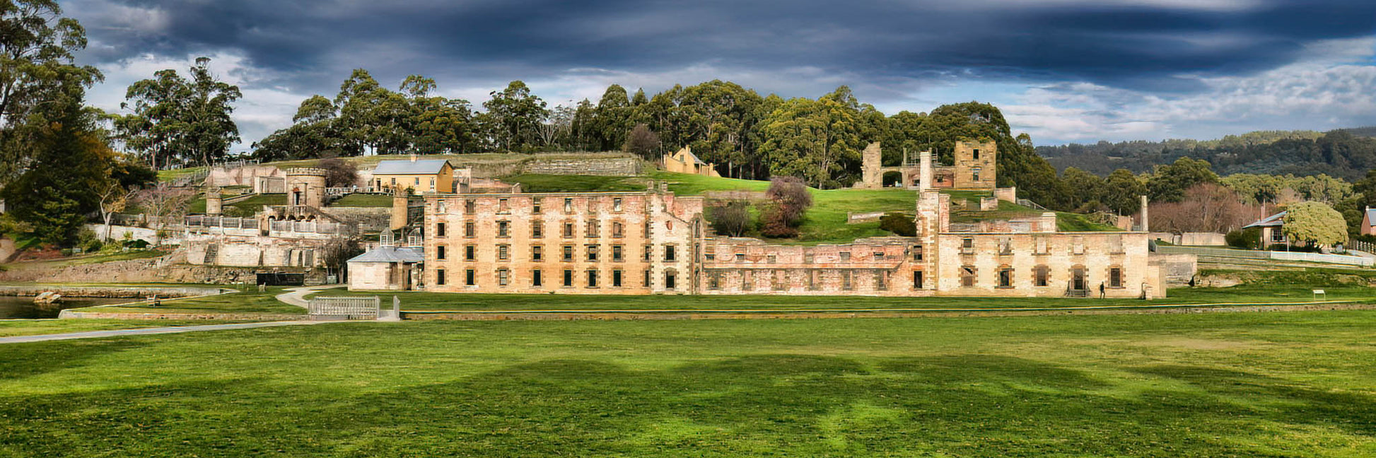 Panoramic view of a historic building at Port Arthur with green grass and trees in the foreground