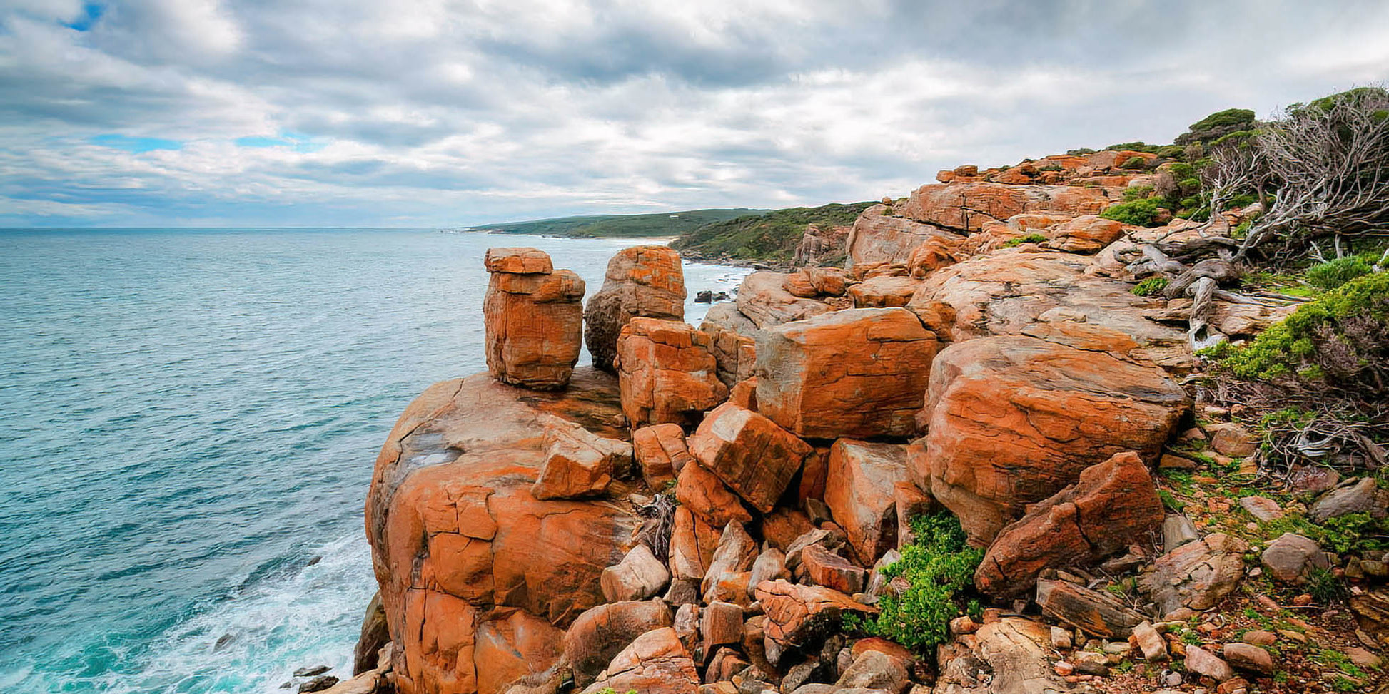 Rugged coastline with orange rocks and blue ocean under a cloudy sky