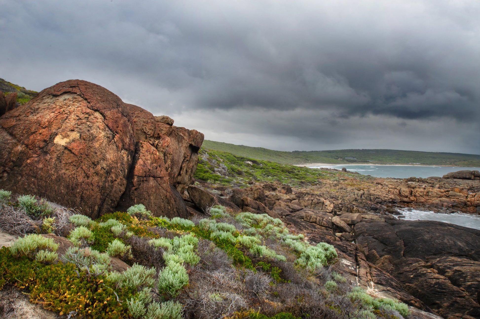 Coastal landscape captured moments before rainfall, with shifting storm layers overhead.