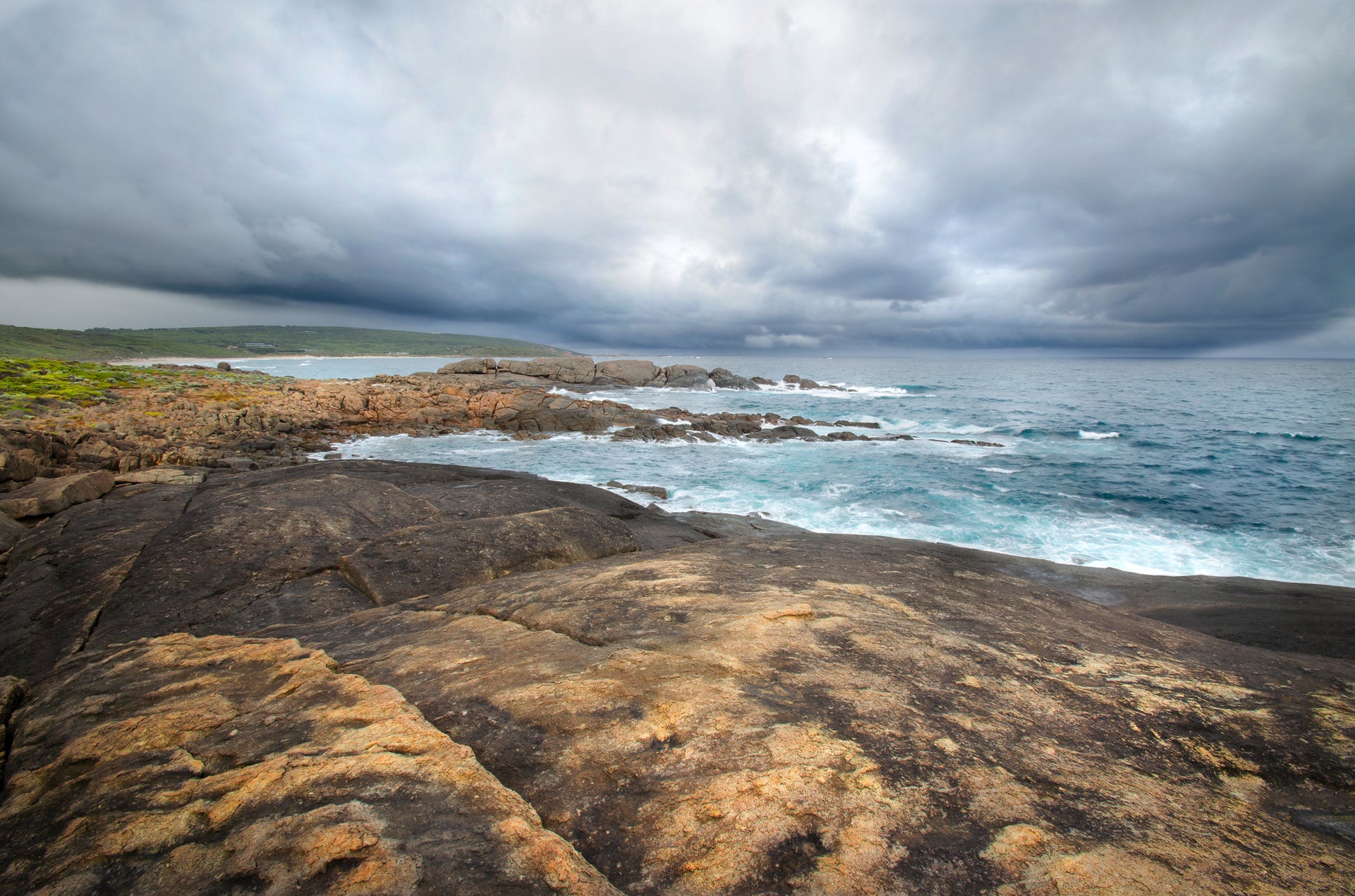 Dramatic storm surge forming under low, brooding clouds with rain falling in the distance at Yallingup.